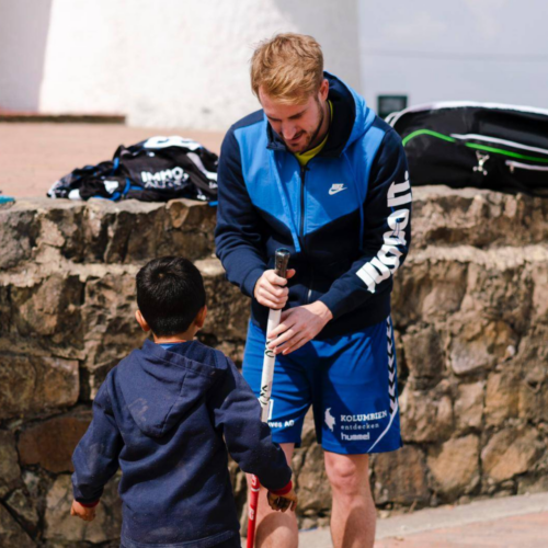 Lukas gibt einem Kind einen Unihockeyschläger.